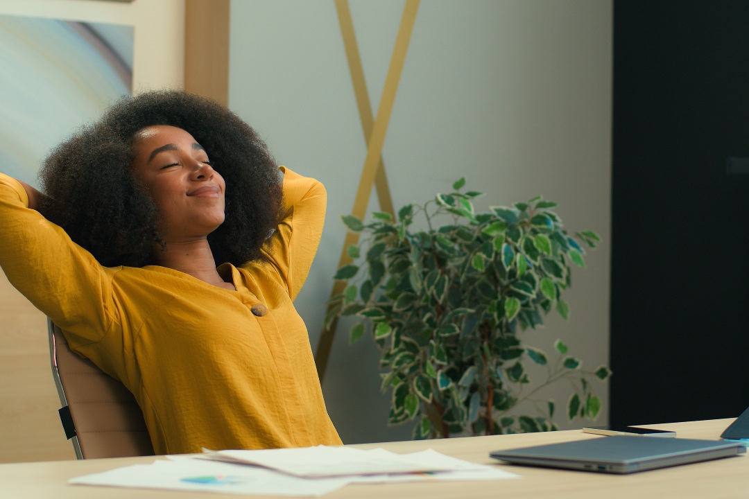 mujer de negocios afroamericana mujer de negocios chica mujer jefa de oficina con portátil en la oficina satisfecha relajada estirándose en la silla descansar poner las manos detrás de la cabeza relajarse realizar trabajo terminar sonreír