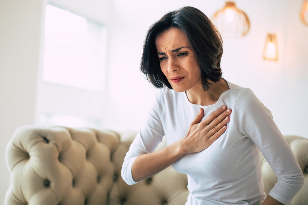 Pressure in the chest. Close-up photo of a stressed woman who is suffering from a chest pain and touching her heart area.