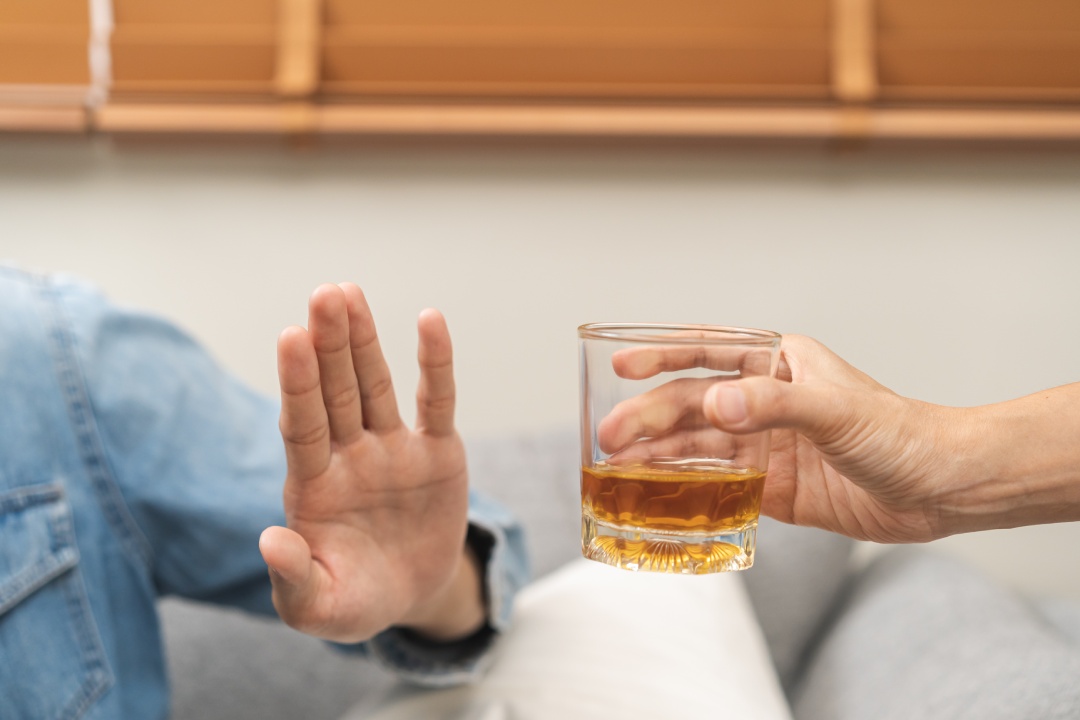 Alcoholismo, joven asiático deprimido se niega, empuja el vaso de bebida alcohólica, bebe whisky, sentado solo por la noche. Tratamiento de la adicción al alcohol, sufrir problema de abuso concepto de alcoholismo.