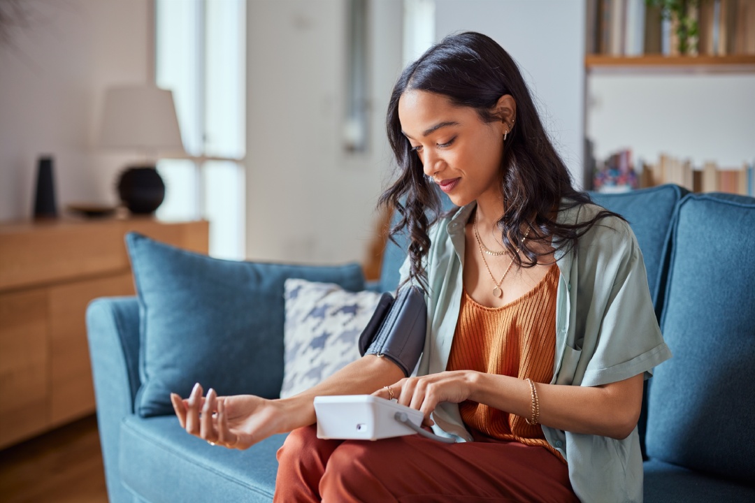 Healthy latin hispanic woman self checking blood pressure using machine. Young mexican woman measuring her own blood pressure with an electronic measurement device at home. Heart rate measurement.