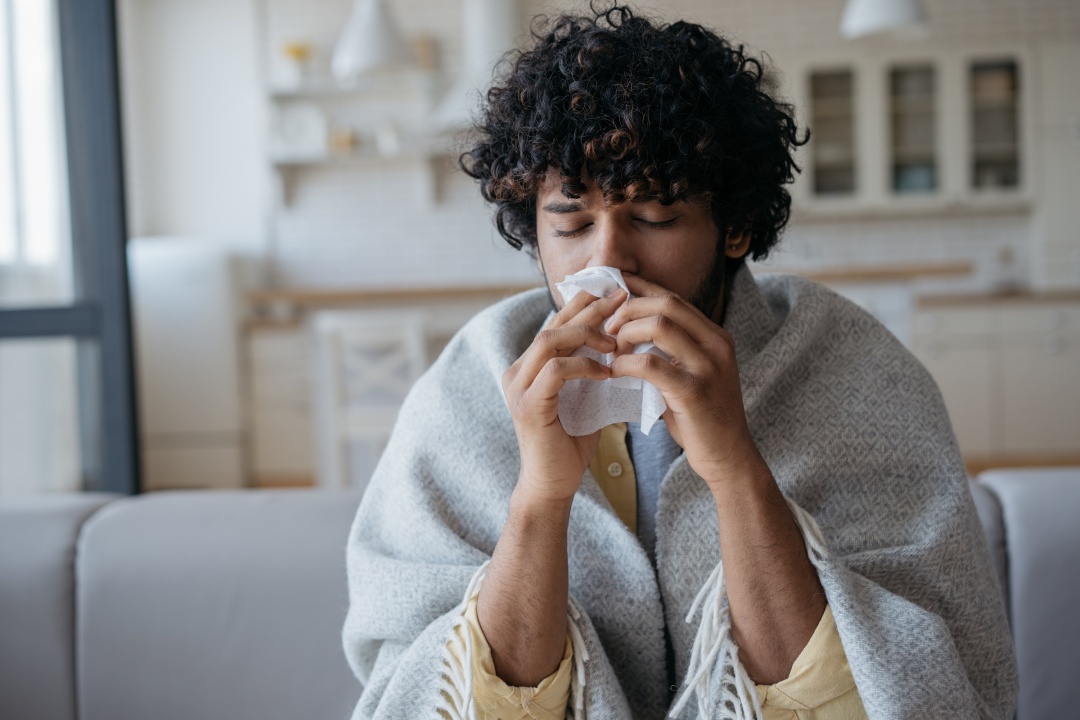 Retrato de hombre indio enfermo con secreción nasal que sostiene servilletas de papel cerca de la cara, sentado en su casa. Concepto de gripe, virus, alergia