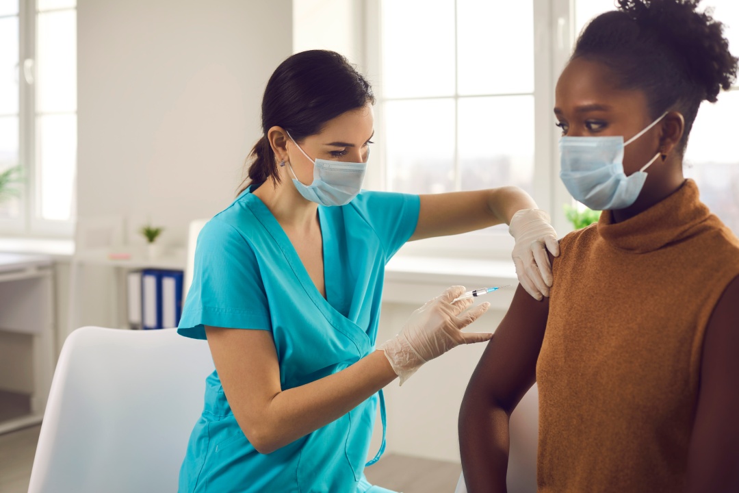 Enfermera profesional o médico con mascarilla y guantes aplicando una inyección a una paciente. Joven afroamericana recibiendo la vacuna contra la gripe o la moderna vacuna Covid 19 durante una campaña de vacunación