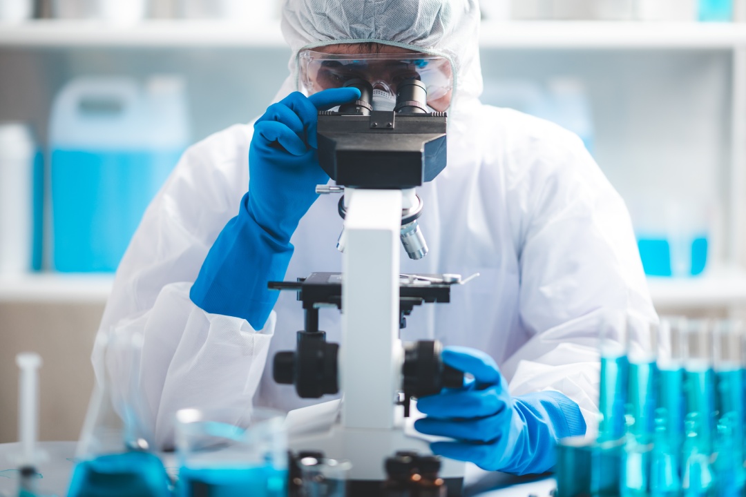 Scientist analyzing microscope slide at laboratory. Young woman technician is examining a histological sample, a biopsy in the laboratory of cancer research